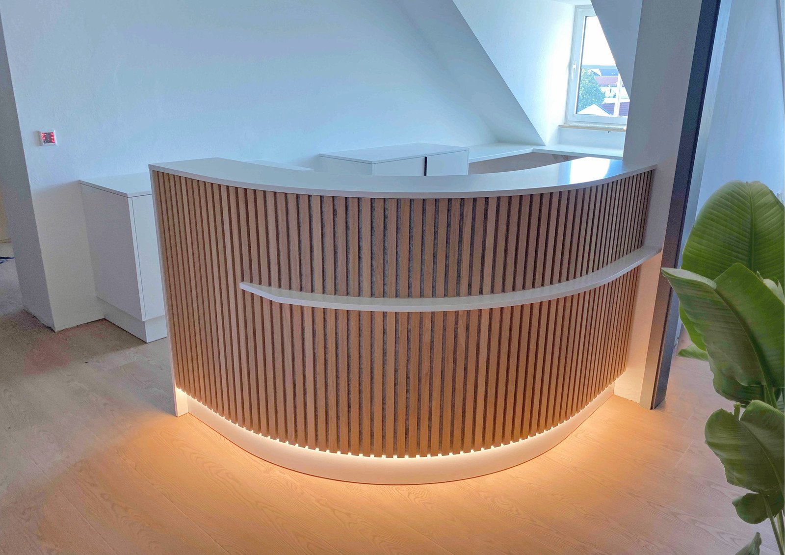 Geschwungener Empfangstresen mit Holzlamellen und Lichtband in einer hellen Praxis unter der Dachschräge