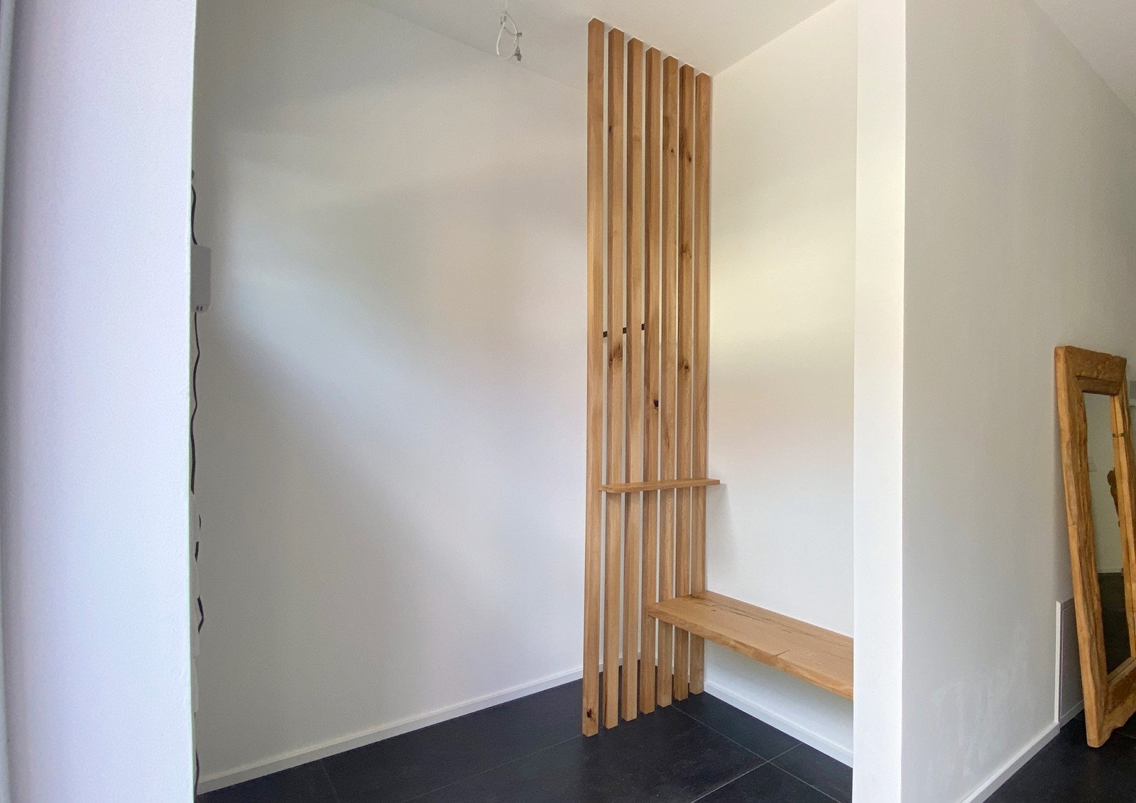 Raumhohe Garderobe aus Eichenlamellen mit Sitzbank vor einer weißen Wand