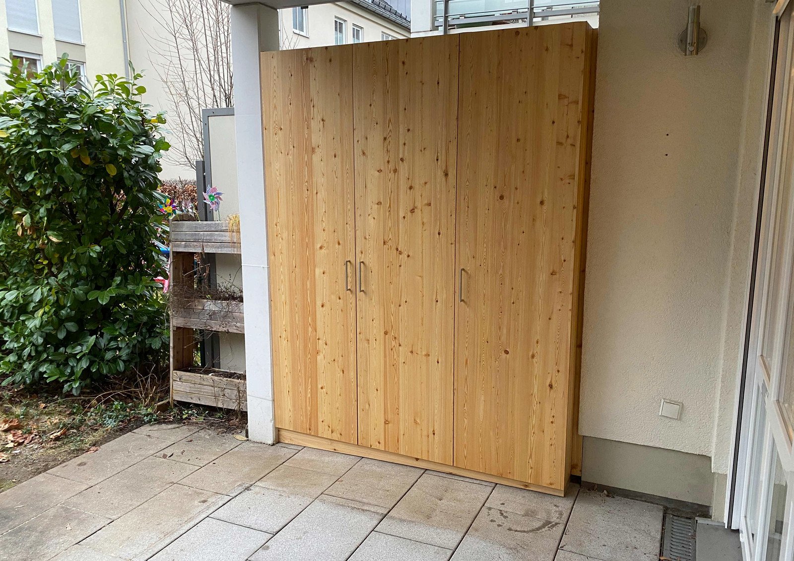 Zweitüriger Gartenschrank aus Lärchenholz an einer Hauswand neben Pflanzen