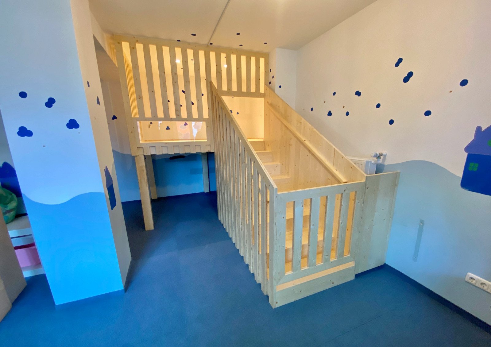 Helle Spielempore aus Holz mit Geländer und Treppe in einem bunt gestalteten Kita-Raum