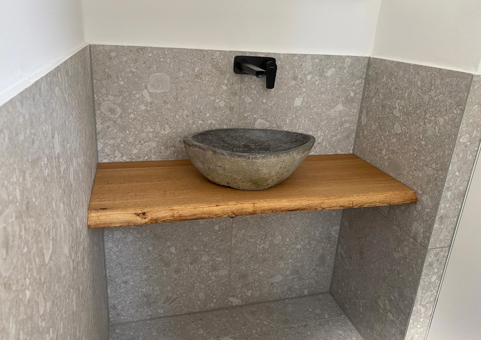 Waschtischplatte aus Eiche mit Baumkante und Aufsatzbecken aus Stein vor grauem Terrazzo